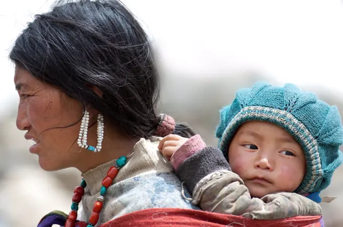 Portrait of Ladakhi woman carrying infant on her back, Phyang, Kardung village, Ladakh, India, June 2010