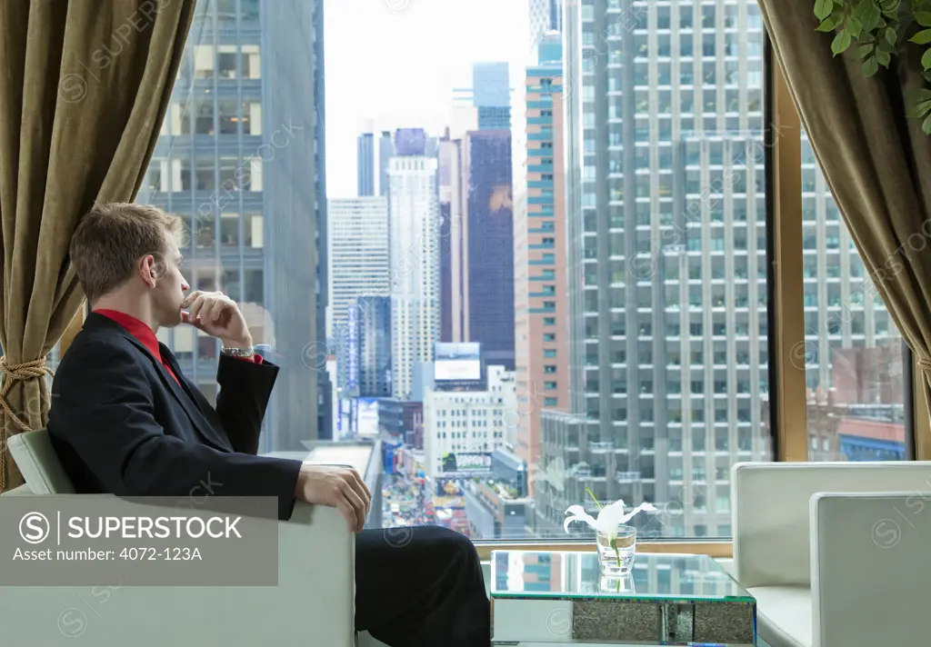 Businessman sitting in the lounge of a hotel and looking out at city through window