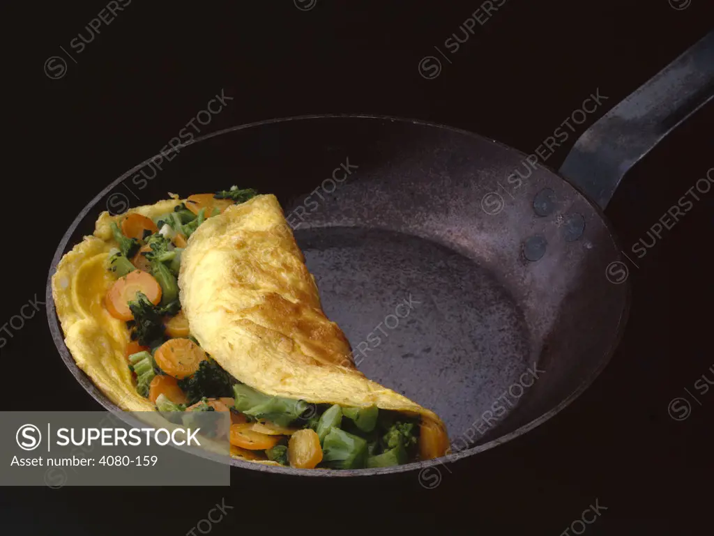 Omelet in a skillet with broccoli and carrots slices