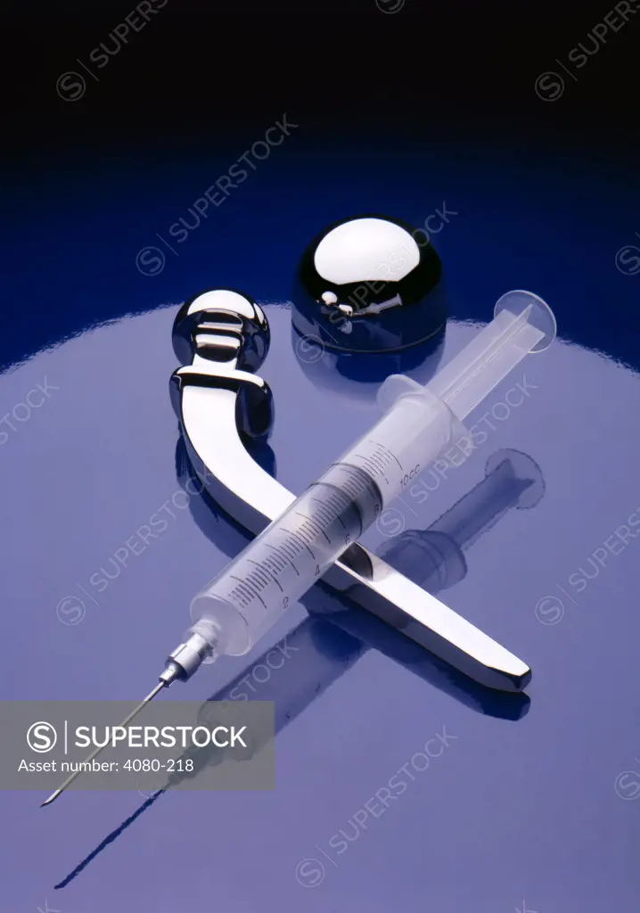 Titanium artificial hip and syringe on shiny blue background, studio shot