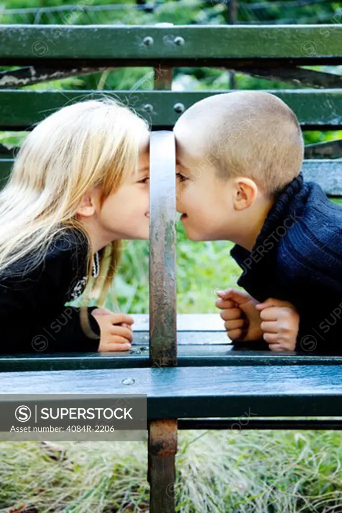 Young Boy and Girl Looking at Each Other Under Park Bench Arm Rest