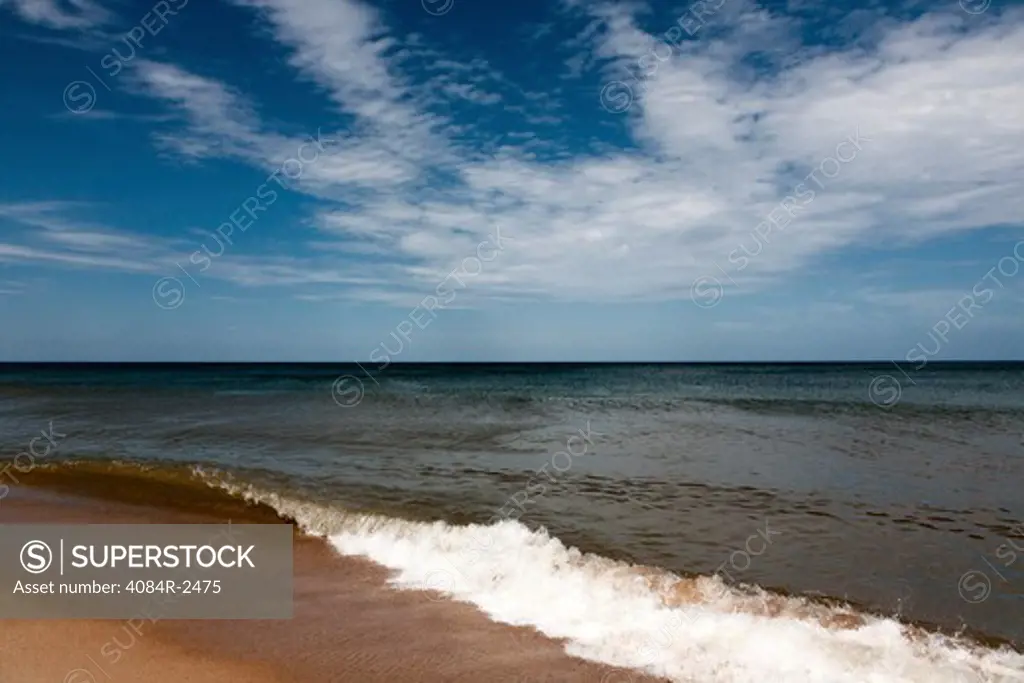 Small Wave Breaking on Shore Against Horizon and Blue Sky