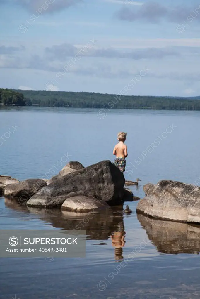 Boy Standing on Rock in Tranquil Lake, Rear View