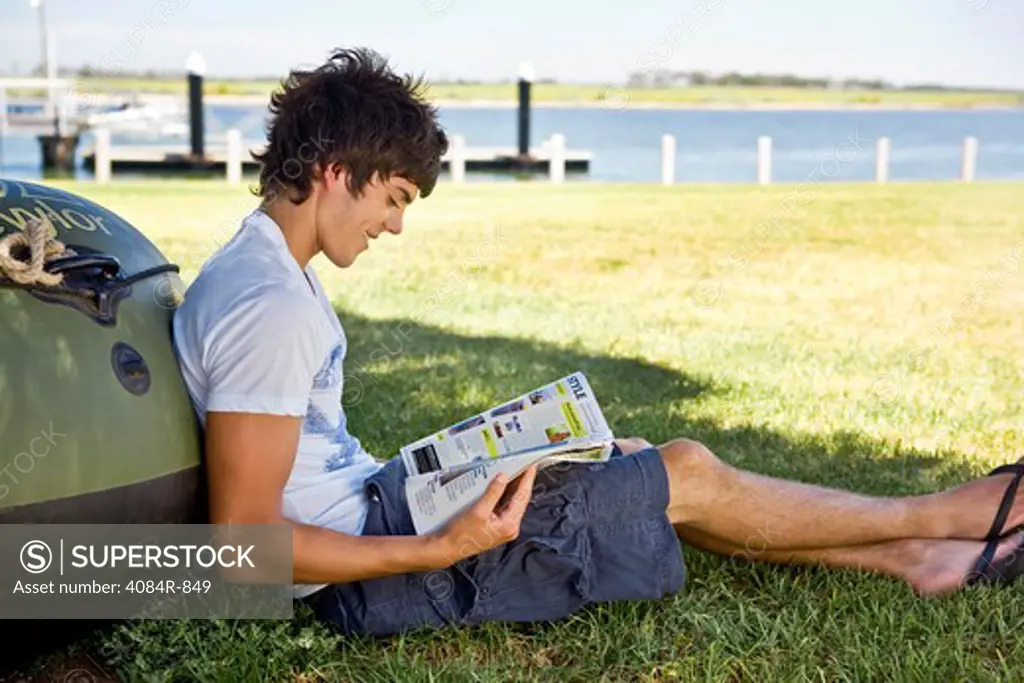 Smiling Young Man Leaning Against Boat, Reading