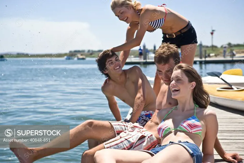 Two Young Couples Sitting on Edge of Pier Having Fun