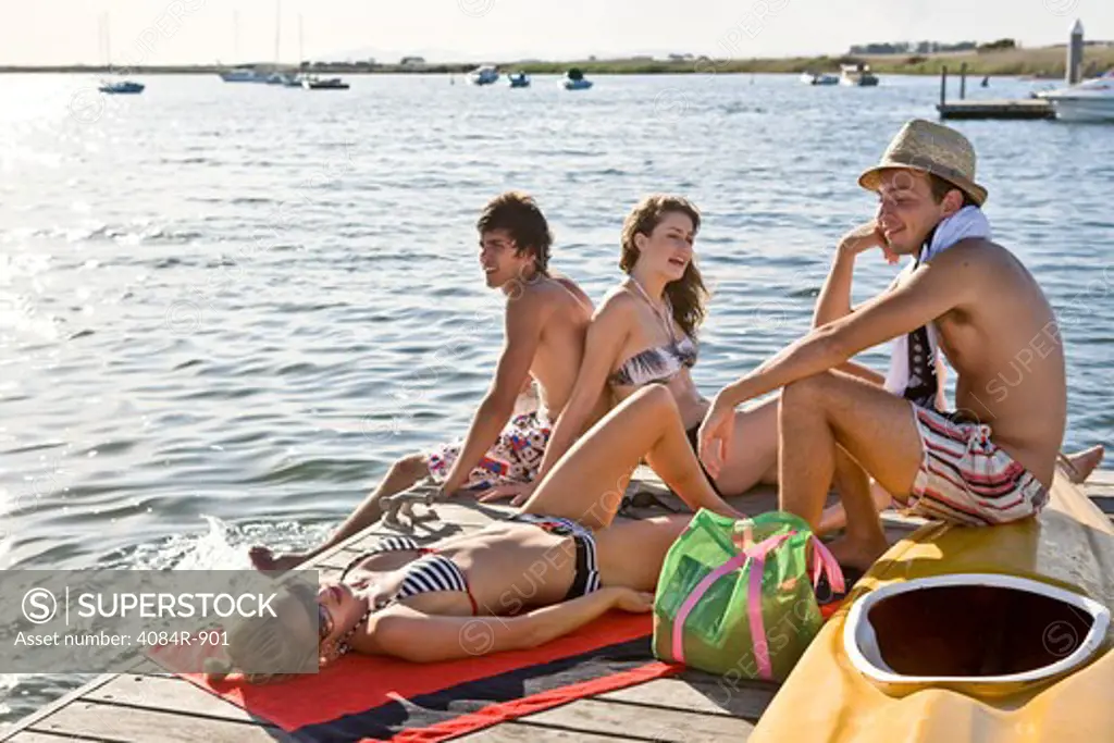 Two Young Couples Sitting and Sunbathing on Edge of Pier
