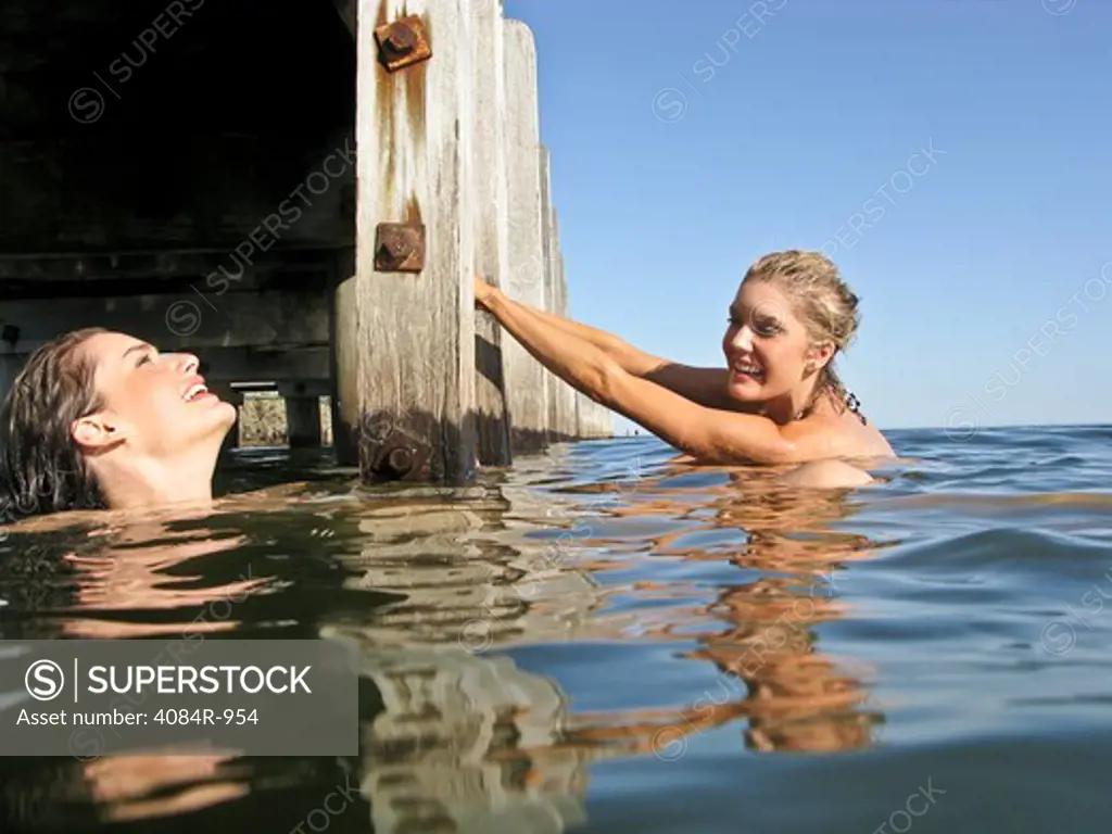 Two Young Women in Water With One Holding onto Pier Steps