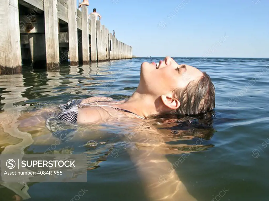 Young Woman Floating in Water Near Pier