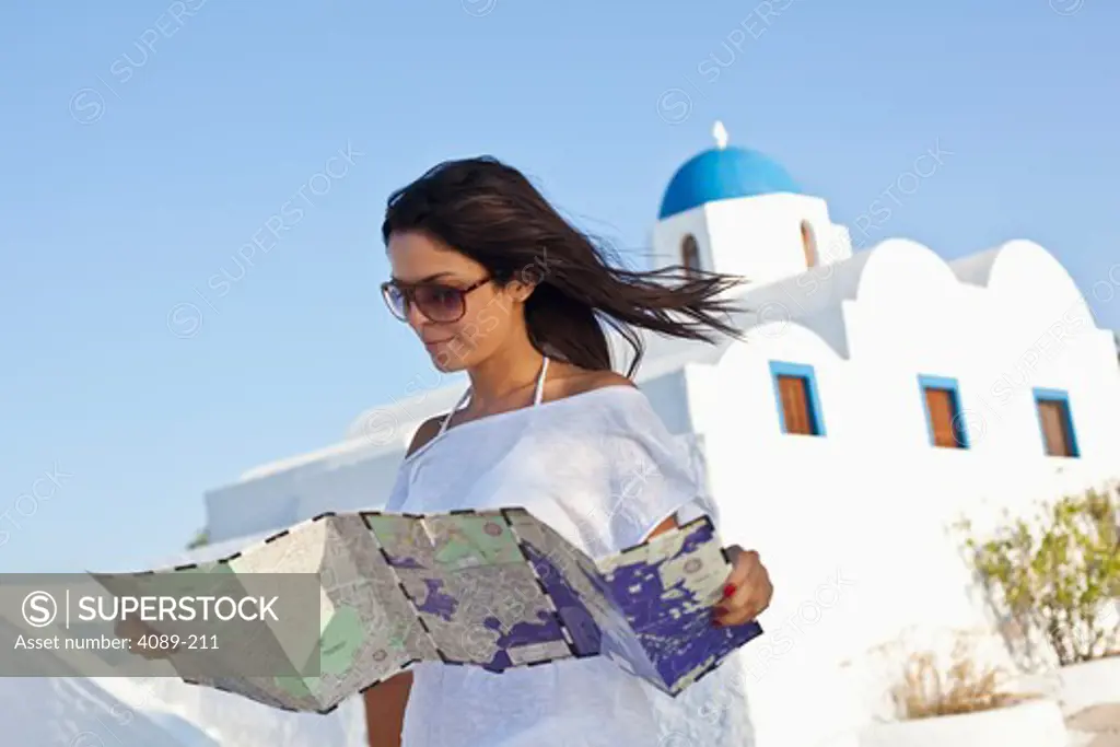 Young woman holding a map with church in the background, Imerovigli, Santorini, Cyclades Islands, Greece