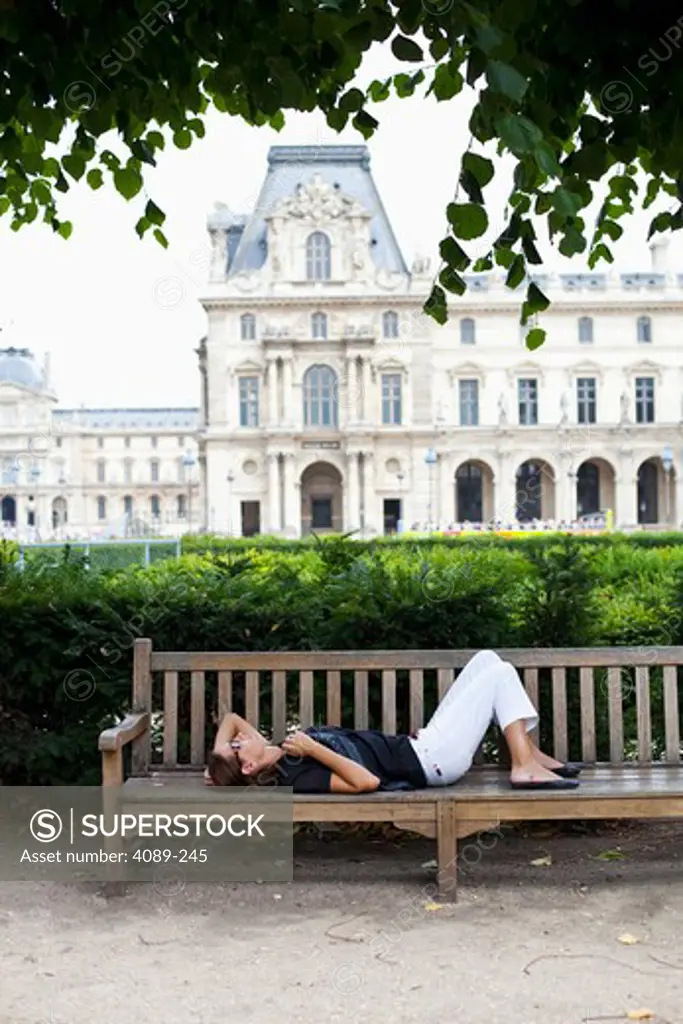 Young woman resting in a garden with a museum in the background, Jardin De Tuileries, Musee Du Louvre, Paris, Ile-De-France, France