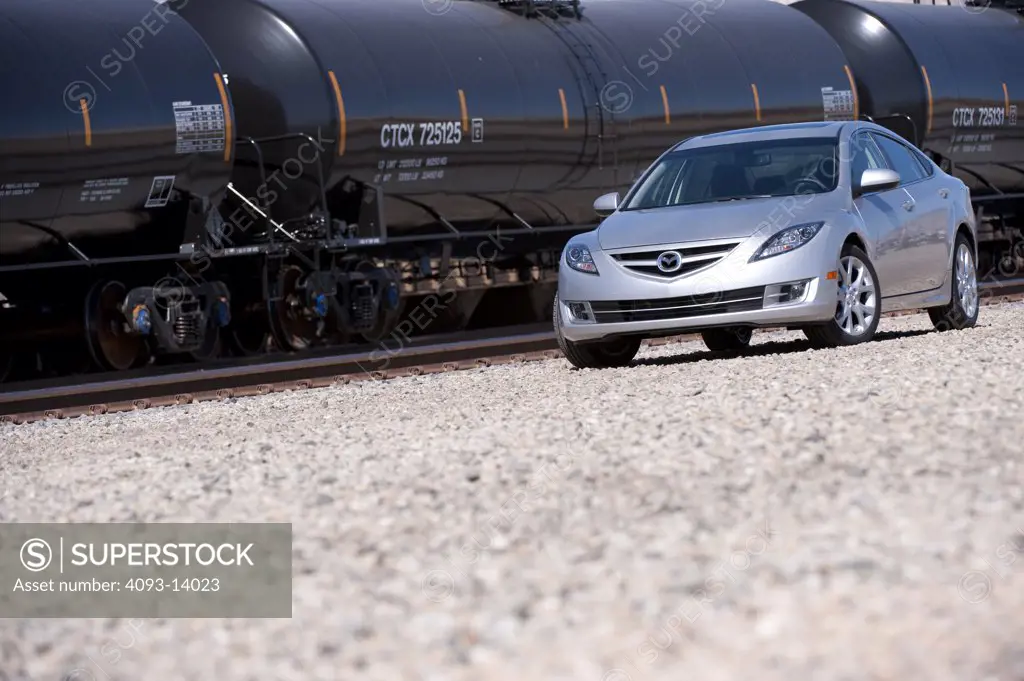 Silver Mazda 6 parked by goods train, side view