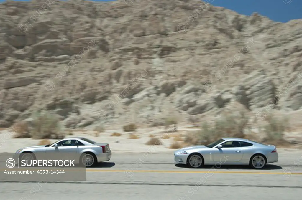 Cadillac XLR-V and Jaguar XKR driving along desert road, side view