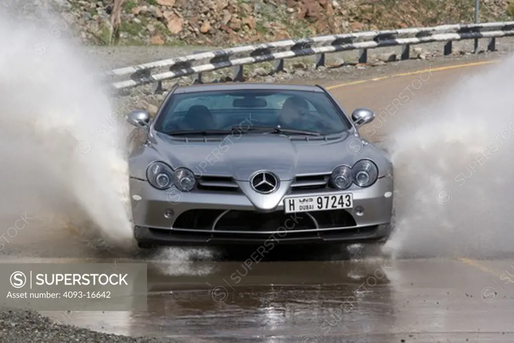 An action shot of a 2007 Mercedes-Benz McLaren SLR 722 going through a low water crossing and throwing a spray of water into the air. The 722 refers to the victory by Stirling Moss and his co-driver Denis Jenkinson in a Mercedes-Benz 300 SLR with the starting number 722 (indicating a start time of 7:22 a.m.) at the Mille Miglia in 1955. The 722 Edition creates 650 bhp, with a top speed of 337 km/h (5 more than the standard SLR). A new suspension is used with 19-inch light-alloy wheels, a stiffer