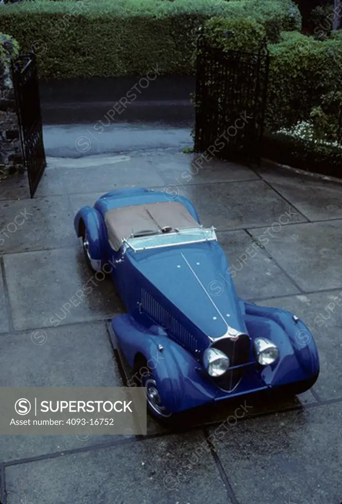 1936 Bugatti Type 57S Roadster beauty front 3/4. The Type 57 S / SC is one of the best-known Bugatti cars. The S stood for surbaissé (lowered), though most felt it stood for sport. It included a v-shaped dip at the bottom of the radiator and mesh grilles on either side of the engine compartment.  Lowering the car was a major undertaking. The rear axle now passed through the rear frame rather than riding under it, and a dry-sump lubrication system was required to fit the engine under the new lo