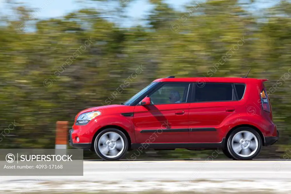 Profile action view of a 2010 red Kia Soul on a rural road