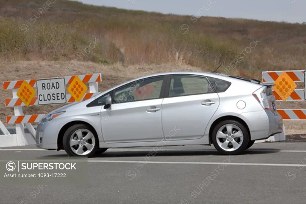 Profile view of a 2010 Toyota Prius Hybrid parked in front of Road Closed barrier signs