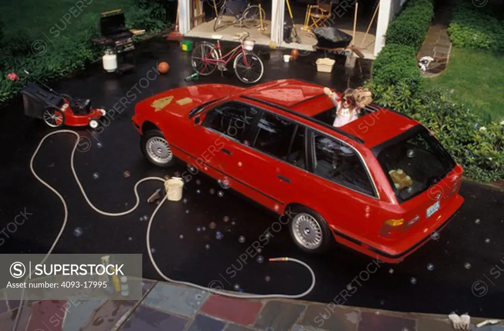overhead high angle BMW 535i 5 Series 1990s red child kid car wash bicycle garden soap hose washing girl driveway street city