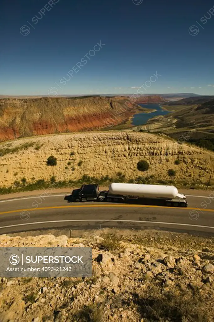 Big diesel truck pulling a tank  with a beautiful view of a canyon.