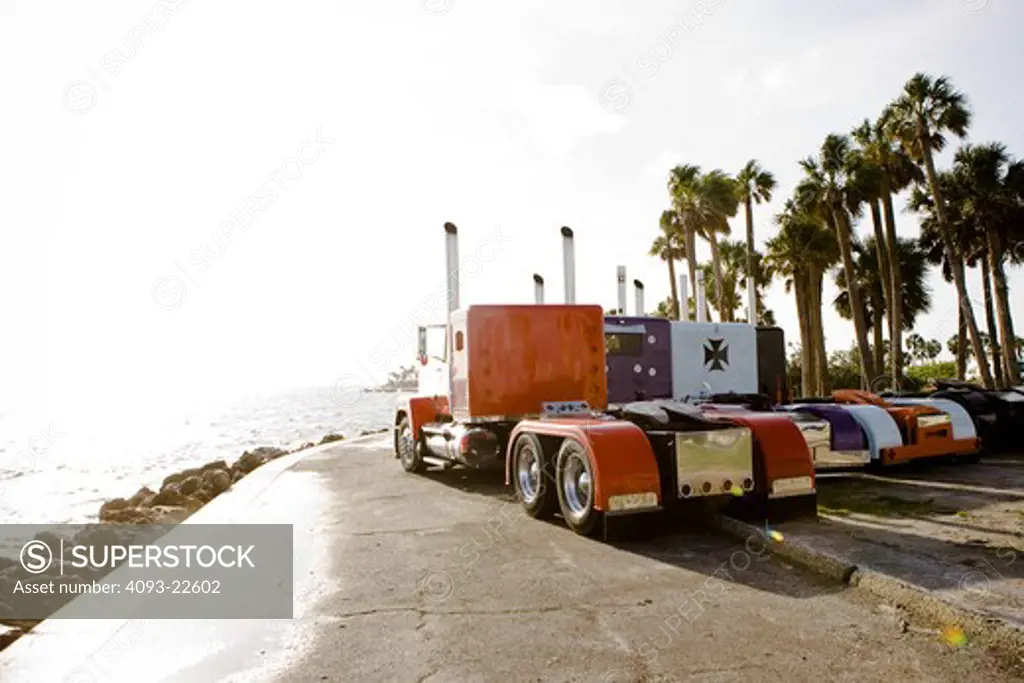 Semi Trucks Big Rig line lined up next to close ocean parked near palm trees