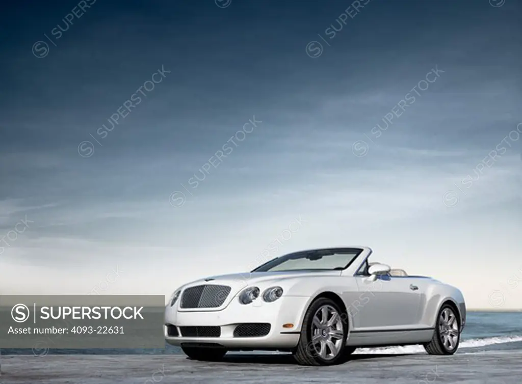 Front 3/4 view of a white 2009 Bentley Continental GTC convertible with the top down at the beach.