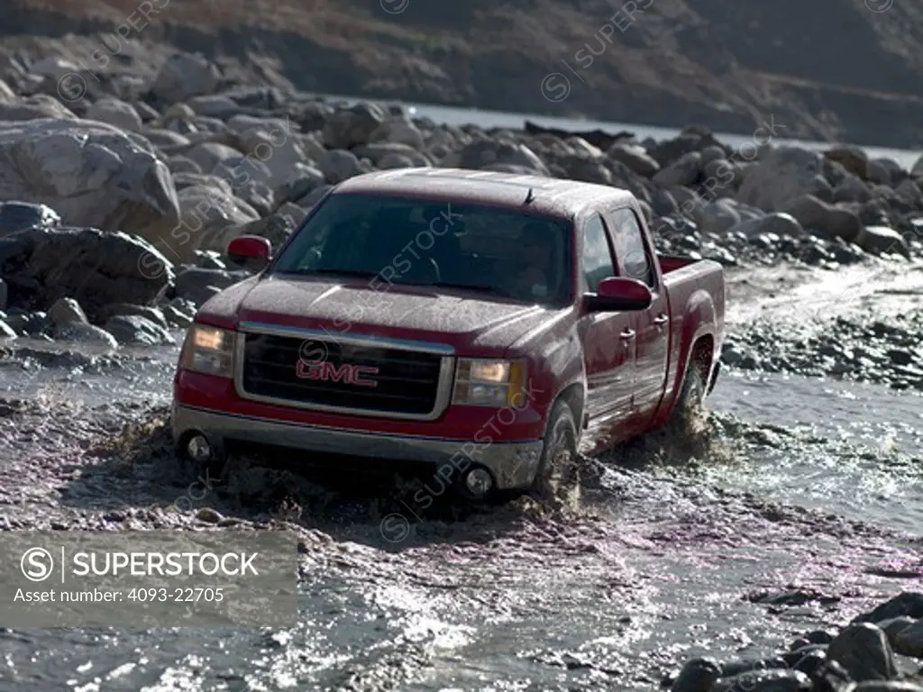 Front 3/4 Action view of a red 2009 GMC Sierra pickup truck driving through mud and water.