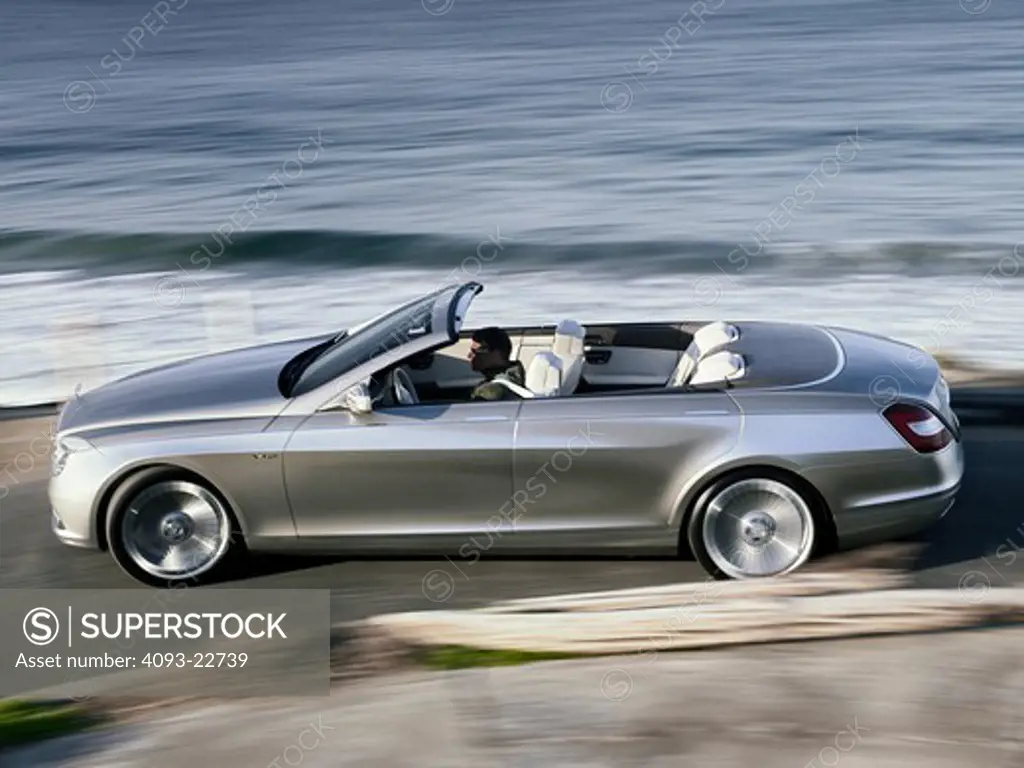 The Mercedes-Benz Ocean Drive is a concept car introduced in 2007. The car is built on the S600 sedan chassis. It's a four door convertible with a soft top. It's not known whether the car will be produced. Profile panning action view of the car on a rural road at the beach.