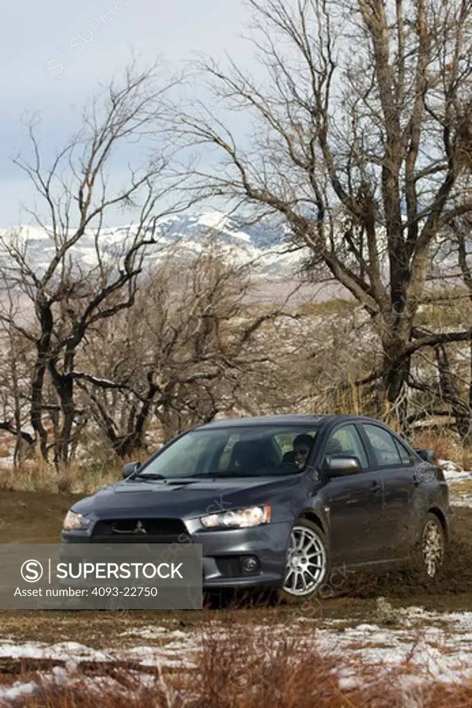 Front 3/4 action view of a 2009 Mitsubishi Lancer EVO X kicking up mud on a rural dirt road.