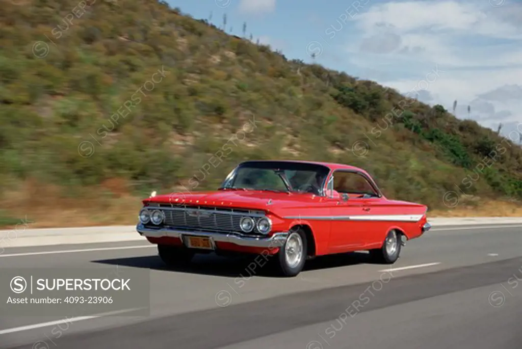 1961 Chevrolet Impala Front 3/4 action of a red 1961 Chevrolet Impala on a public highway.
