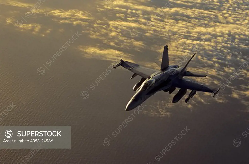 US Navy VFA-115 Boeing F/A-18C Hornet above the Pacific Ocean and clouds near Hawaii in warm evening light, sunset