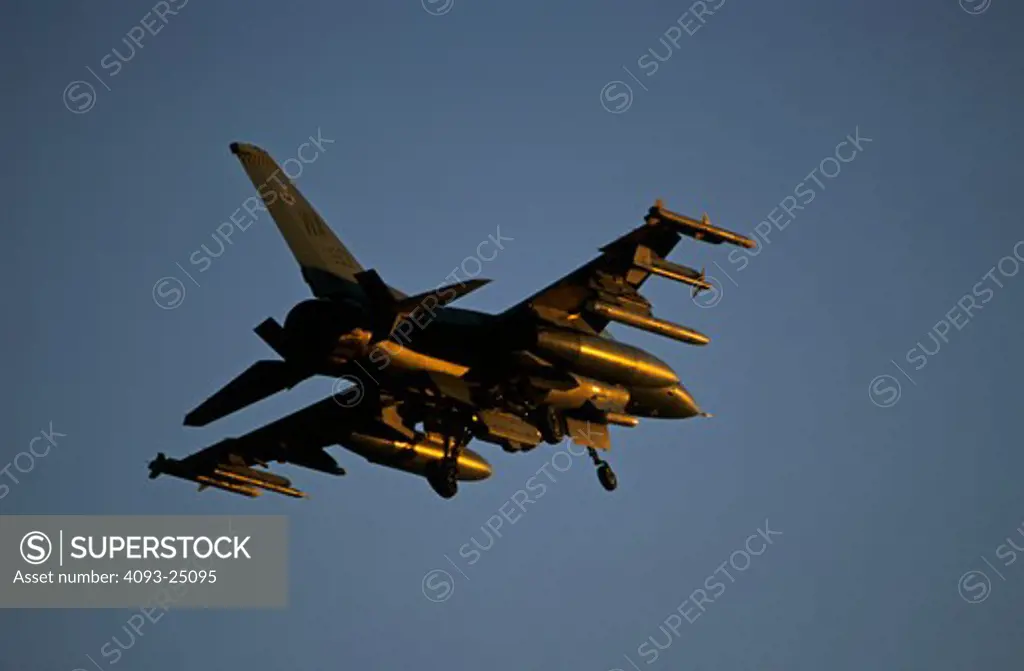 Lit with a golden glow of the setting sun, a USAF F-16 Fighting Falcon (Viper) on final approach. Ordnance includes air to air Sidewinder and AMRAAAM missiles