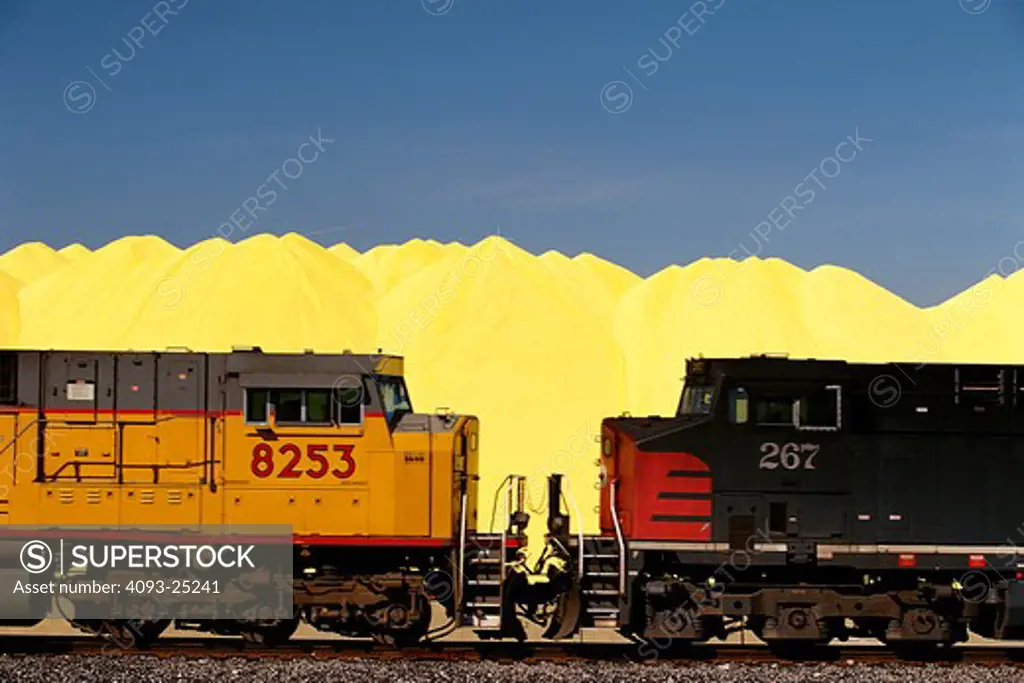 Union Pacific coal train passes a mountain of yellow sulfur (or sulpher) at an outdoor storage yard near the Port of Long Beach  Calif. Locomotives seen in photo are Union Pacific # 8253  an EMC SD9043AC and Southern Pacific # 267  a AC 440-CW built by GE Transportation Systems of Erie  Pennsylvania. 2-19-2002