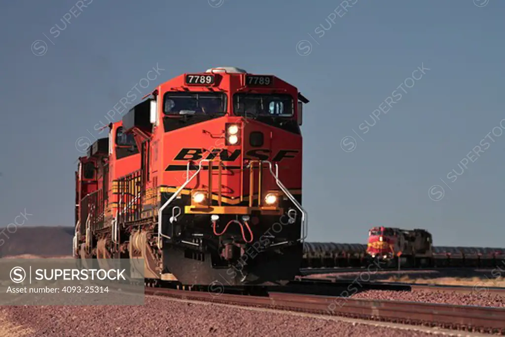 BNSF diesel electric locomotive # 7789 manufactured by General Electric model ES44DC at Goffs California with a coil steel train in tow. A second BNSF train wearing the old Santa Fe warbonnet paint colors is seen in the background hauling a load of empty well cars that will be loaded with containers in the LA or Long Beach harbors.
