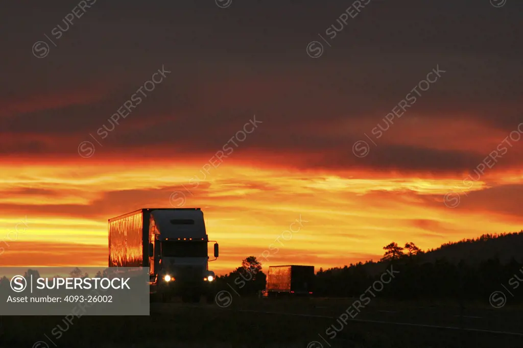 Big Rig Semi Truck driving on the freeway highway road very dramattic sunset bright orange clouds