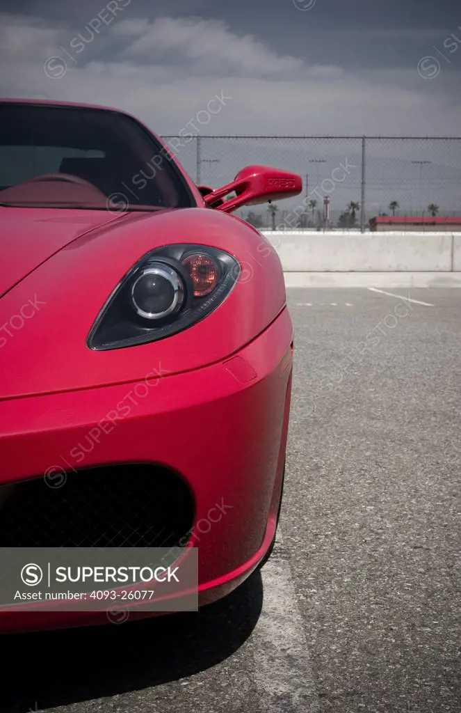 2006 Ferrari F430 parked in empty parking lot next to a wall and fence showing close up of headlight and side view mirror