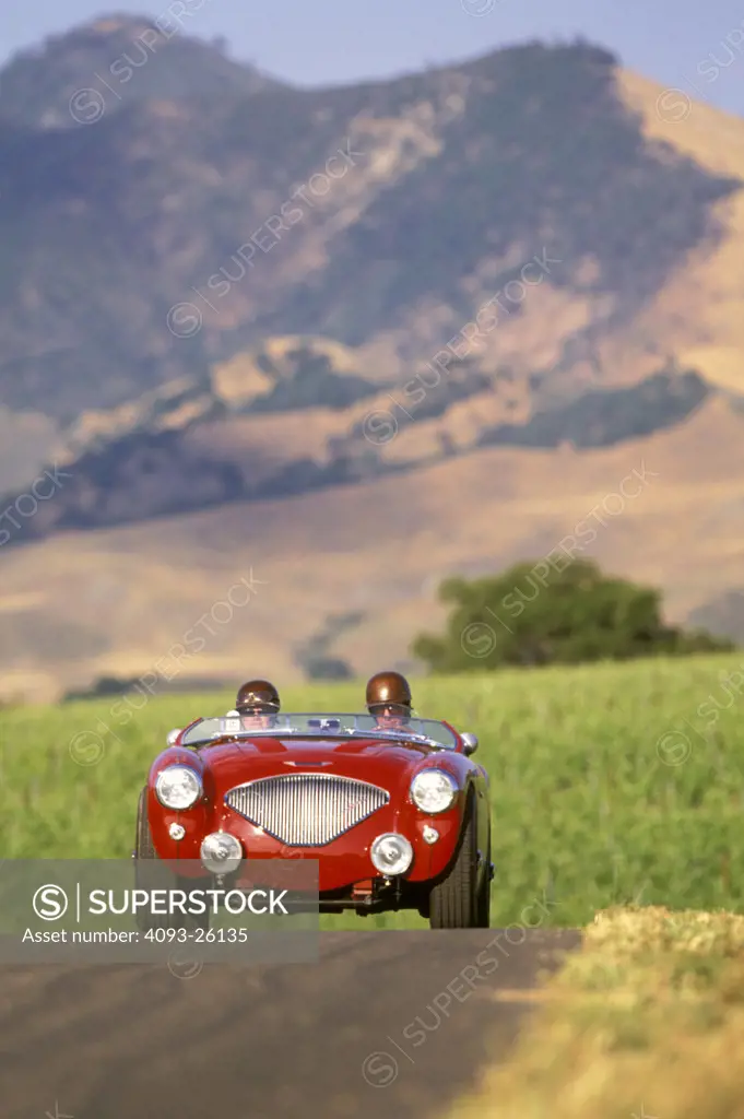 austin-healey 100 1954 old style classic couple ride helmets glasses mountains background