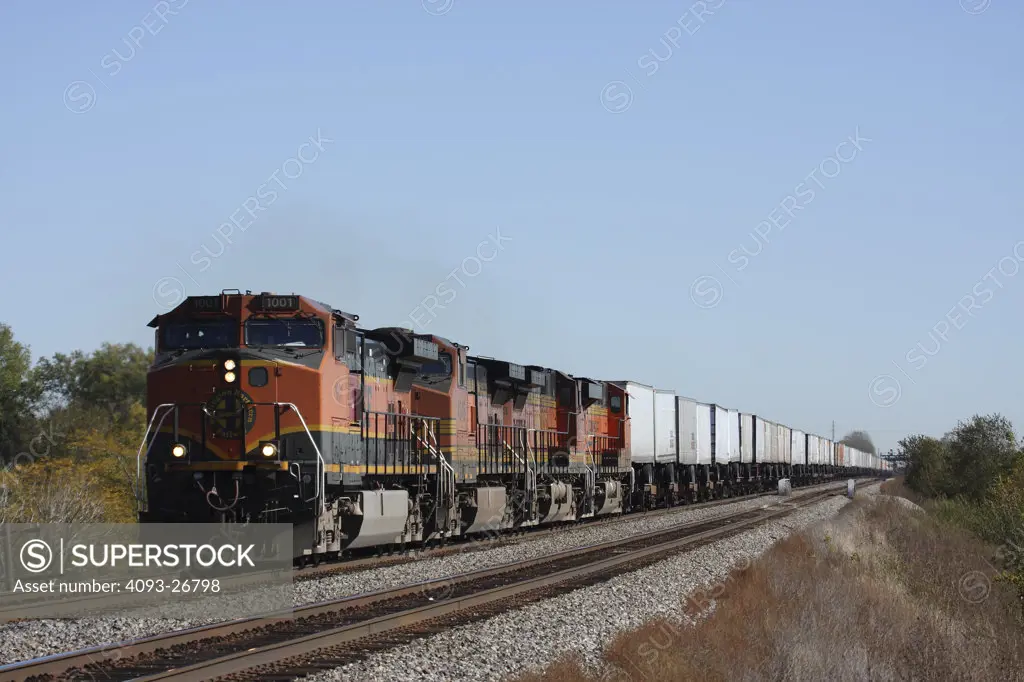 BNSF1001 Intermodal w/ 4 engine consist, General Electric C44-9W, westbound,  metal semi trailers, rural setting, blue sky, ditch lights on