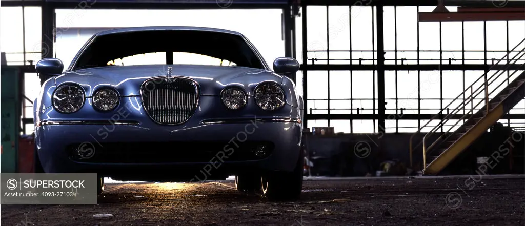 2006 Jaguar XK8 Xk-8 inside a large garage with the sun peaking from the bottom of the car in an industrial area