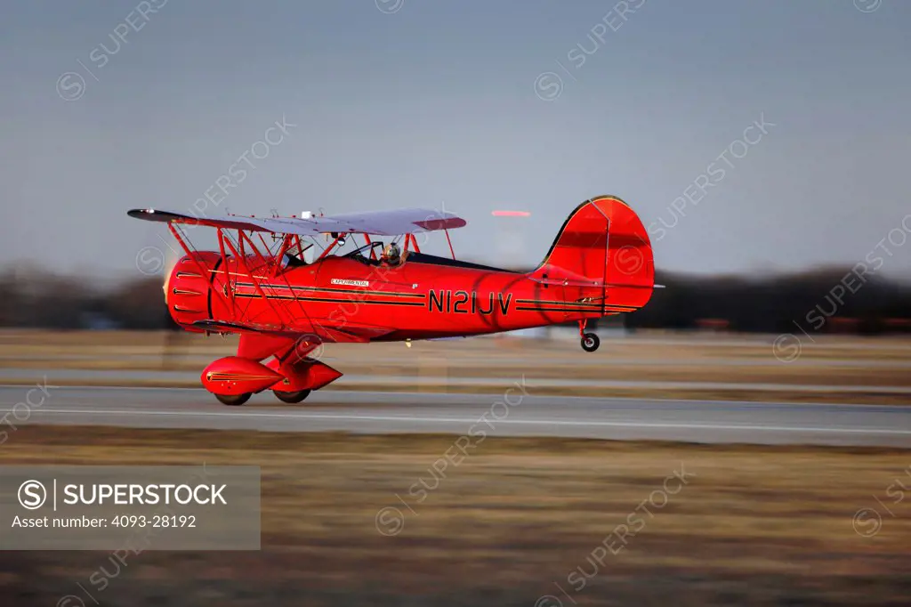 Action view of a red 2010 Waco YMF-5D on the take off roll on a rural runway at dusk, side view