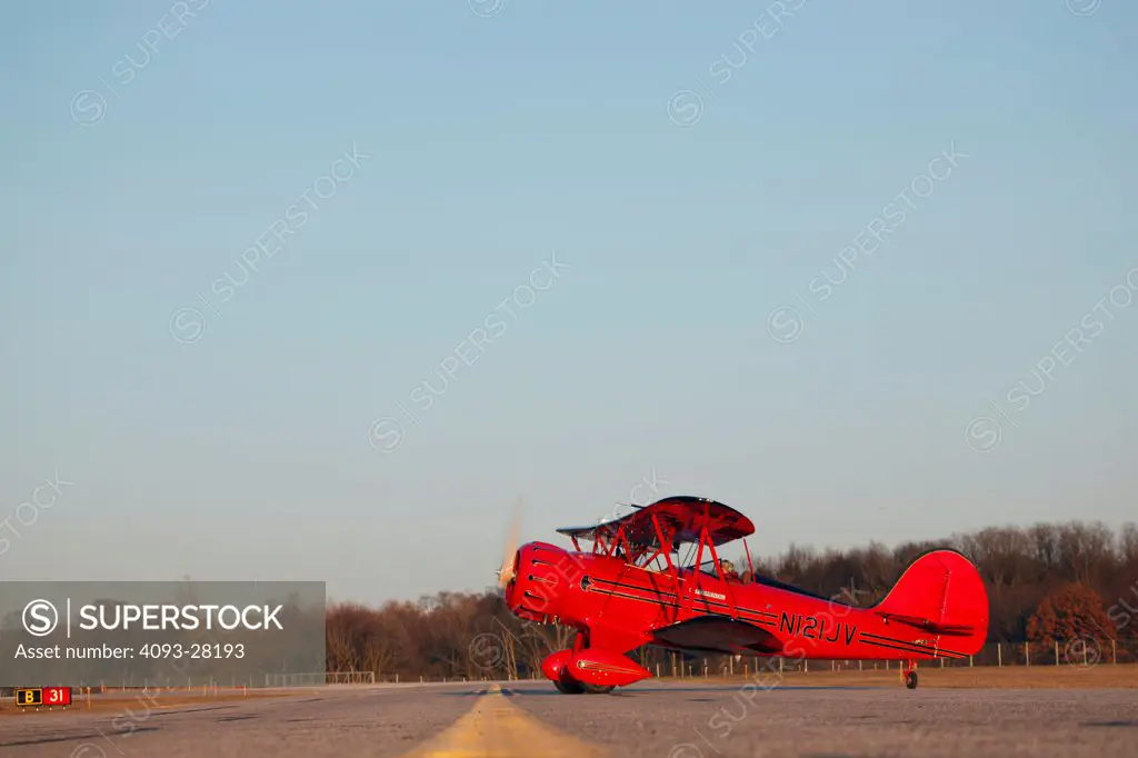 Bright red 2010 Waco YMF-5D parked on a rural airstrip at dusk, side view