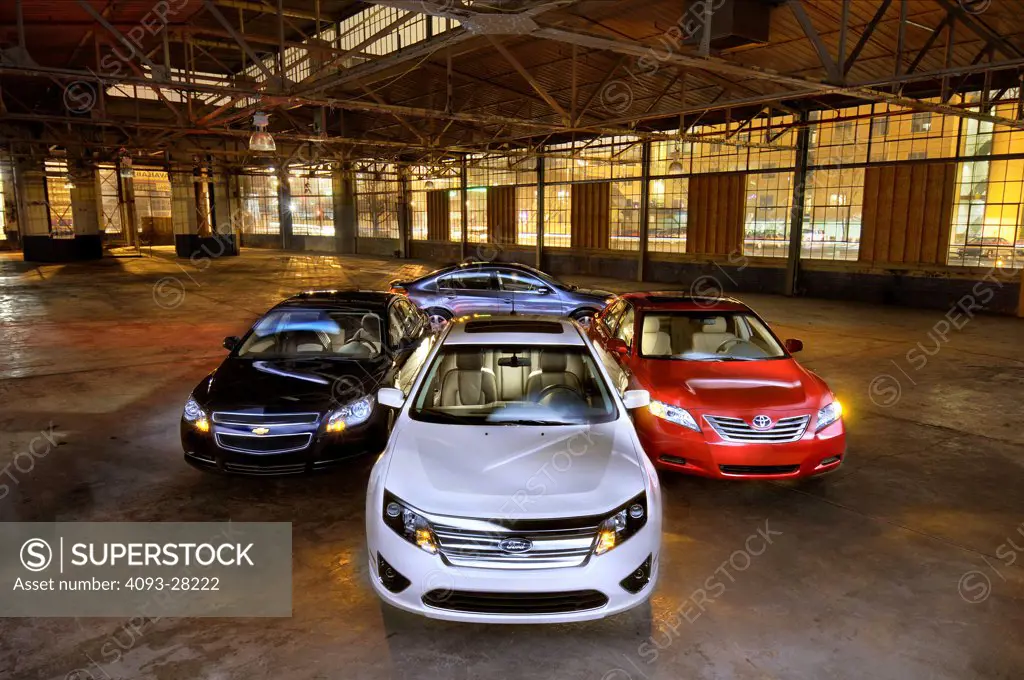 2010 Ford Fusion, 2010 Camry Hybrid, 2010 Altima Hybrid, and 2010 Malibu Hybrid sedans in industrial building, front view