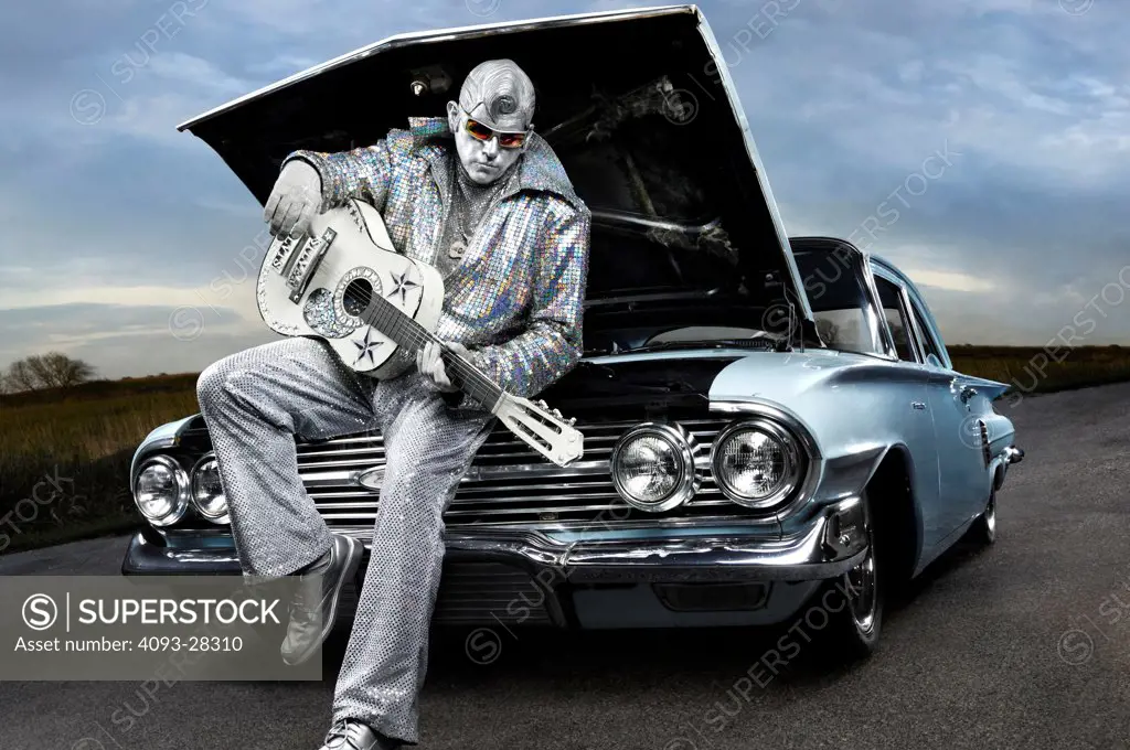 Silver Elvis impersonator, street performer with a guitar sitting on the front of a 1960 Chevrolet Impala