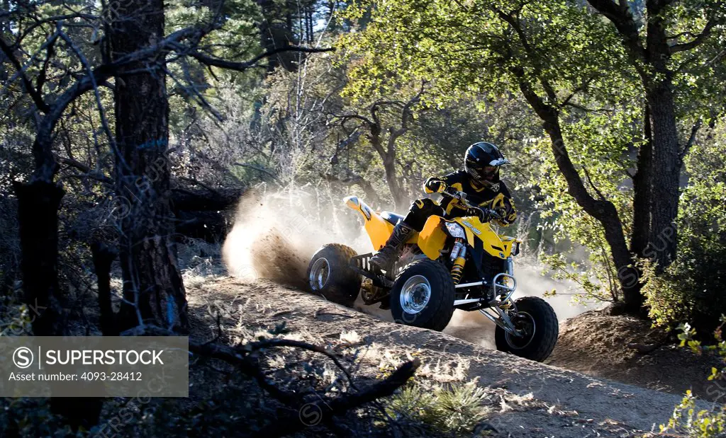 Front 3/4 action of a yellow 2010 Can-Am Quad ATV on a rural, tree lined trail