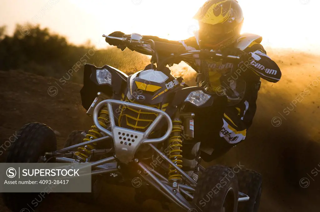Front 3/4 action of a 2010 Can-Am Quad ATV kicking up dirt on a rural trail at sunset