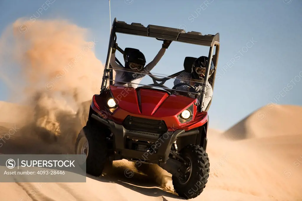 Front 7/8 action of a red 2010 Kawasaki Teryx Quad ATV kicking up sand on a large sand dune in the late afternoon