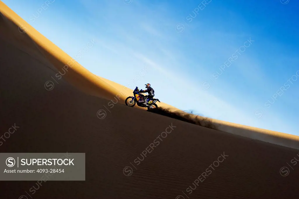 Profile action of a motorcycle racer on a large sand dune in the Dakar Rally of 2010