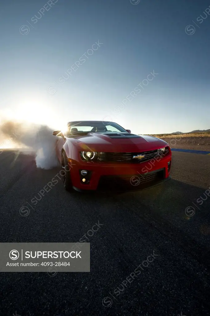 Front 7/8 action of a 2013 Chevrolet Camaro ZL1 doing a smoky burnout on a rural road in the desert