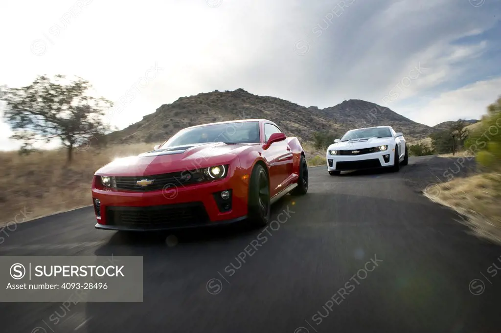 Front 3/4 action of two 2013 Chevrolet Camaro ZL1 sports cars on a rural mountain road