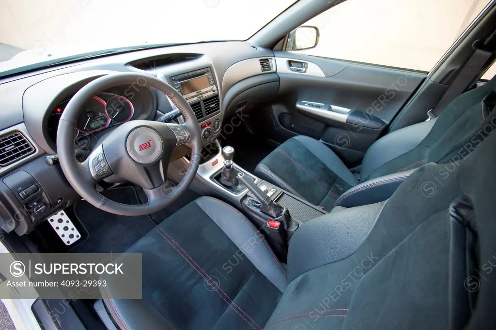 Interior view of a 2012 Subaru Impreza WRX STI showing the steering wheel, instrument panel, dashboard, center console, gear shift lever, emergency brake and deep bucket seats.