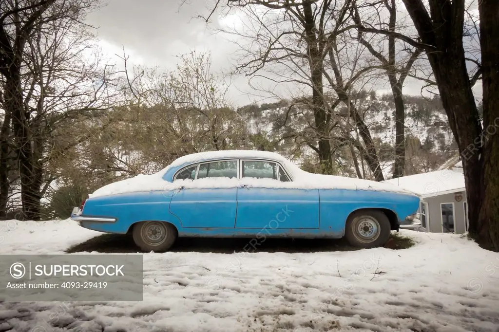 Static profile of a blue 1961 Jaguar Mark X parked in a rural snow covered location.