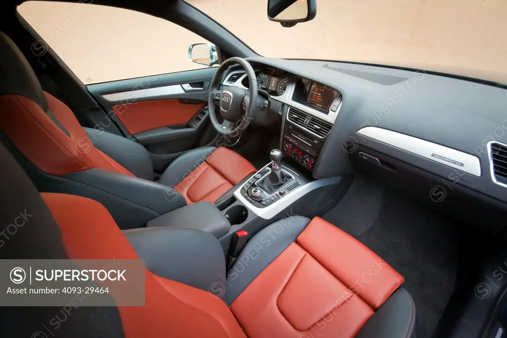 Inerior view of a 2012 Audi S4 showing the steering wheel, instrument panel, center console, multi function display, dashboard, GPS Navigation System, manual gear shift lever and red and gray leather seats.
